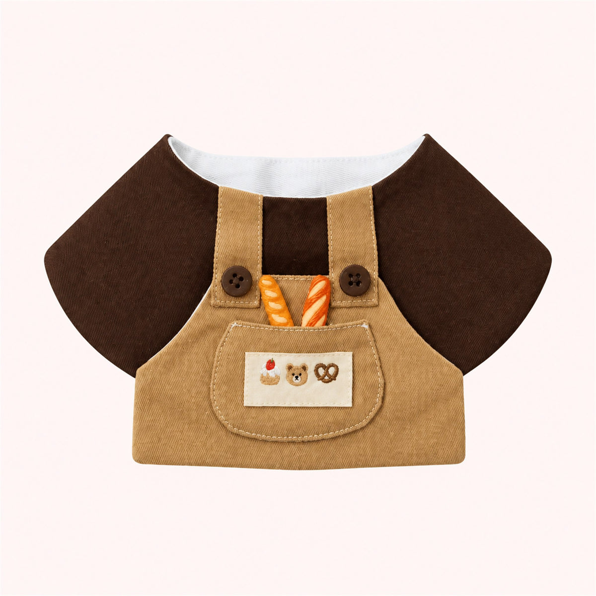AI-cleaned product photo: Little Baker Pet Bib — Chocolate-and-khaki overalls with two mini baguettes in the pocket and a bear-cookies patch.