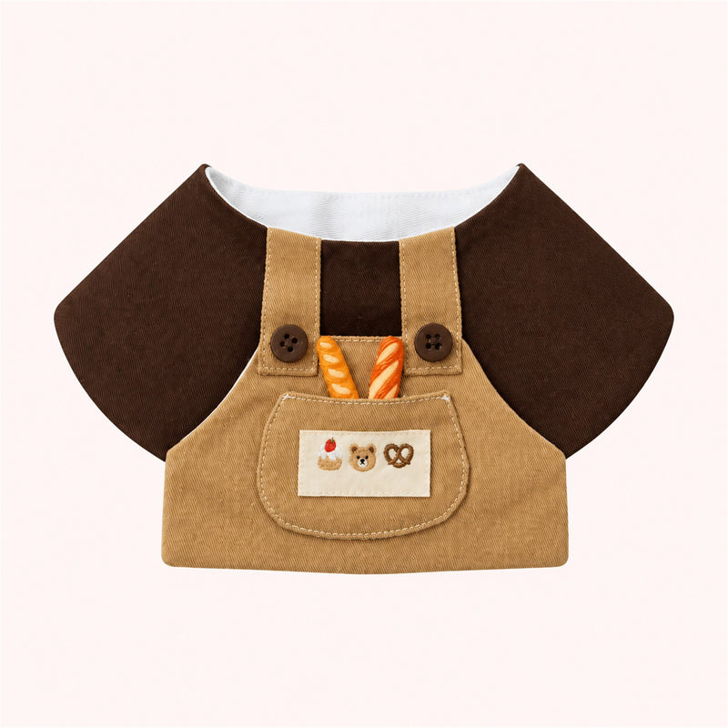 AI-cleaned product photo: Little Baker Pet Bib — Chocolate-and-khaki overalls with two mini baguettes in the pocket and a bear-cookies patch.