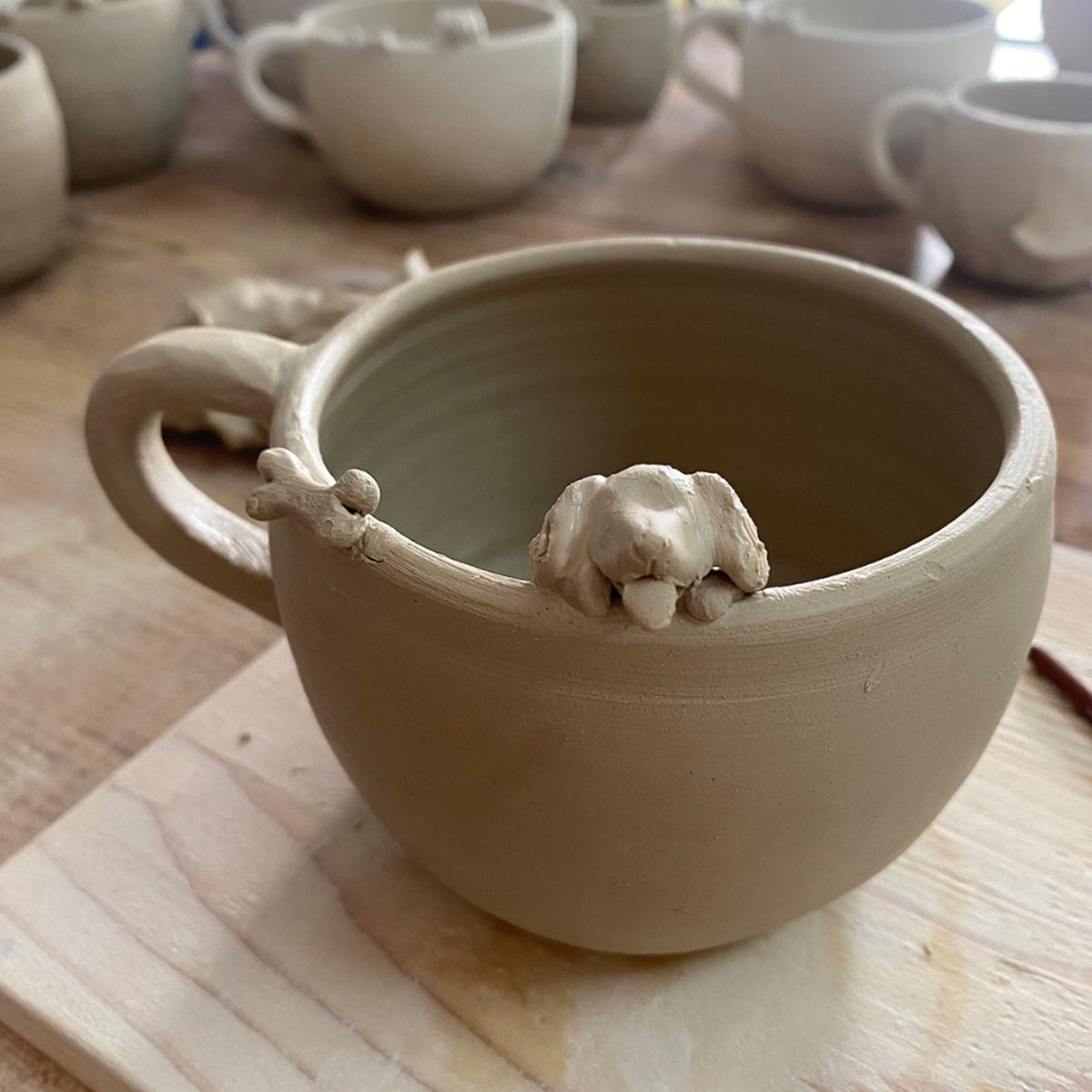 AI-cleaned product photo: hand-sculpted dog figure on an unglazed clay mug in the studio